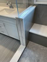 Bathroom with white vanity, marble-tiled wall with a bench, and gray hexagonal floor tiles.