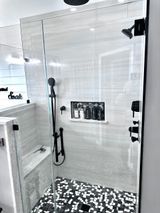 Modern shower with glass walls, black fixtures, stone floor, and built-in bench.