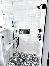 Modern bathroom shower with glass doors, black fixtures, and mosaic tile floor.