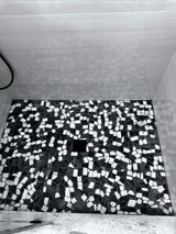 Black and white mosaic tile shower floor with central drain, in a shower stall.