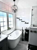 Modern white bathroom with freestanding tub, large window, and decorative pendant light.