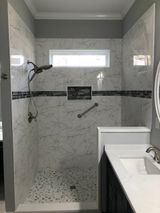 Accessible shower with stone floor and grab bar, built-in shelf, light-colored tile, and dark accent stripe.