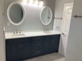 Bathroom with navy blue vanity, white countertop, oval mirrors, and gray walls.