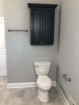Bathroom with gray walls, white toilet, dark cabinet, and chrome towel bars.