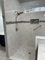 Shower with marble-look tile, mosaic floor, handrail, and built-in niche. A window is above.