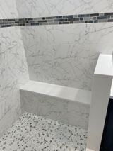 Marble-tiled shower with a built-in bench. The floor has a speckled mosaic pattern. A decorative tile border is above.