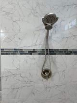Shower with handheld sprayer on white marble-look tiled wall with a dark tile accent.
