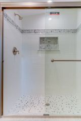 Shower with glass door, white tiled walls and pebble-stone floor.  Silver fixtures.