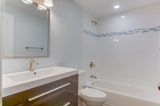Bathroom with white walls, brown vanity, white sink, and bathtub; light blue tile border.