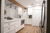 White kitchen with island, cabinets, and appliances; wood beam and floor.
