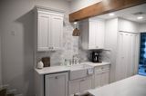 White kitchen with cabinets, sink, and coffee maker. Rustic wood beam overhead.
