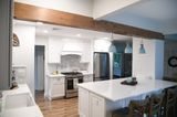 White kitchen with island, stainless steel appliances, and wooden beam.