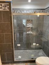Bathroom with gray tile shower, glass door, built-in shelves, and decorative mosaic accents.