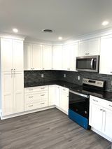 White kitchen with dark countertops, stainless steel appliances, and gray flooring.