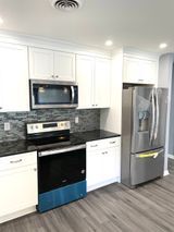 White kitchen cabinets, stainless steel appliances, black countertop, blue dishwasher cover, and grey floor.