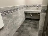ADA accessible restroom with a lowered sink, gray tile walls and floor, and a soap dispenser.