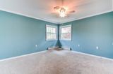 Empty room with blue walls, two windows, beige carpet, and a ceiling fan.