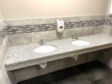 Public restroom with two sinks, granite countertop, and decorative tile backsplash.