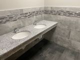 Bathroom with two sinks set in a gray granite countertop, gray tiled walls and floor.