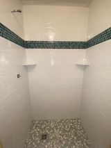 Shower with white tiled walls, blue mosaic border, pebble floor, and white shelves.