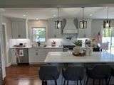 Modern kitchen with light gray cabinets, white countertops, and three pendant lights over a white island with gray bar stools.