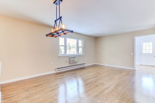 Empty dining room with hardwood floor, window, and modern chandelier.
