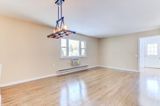 Empty living room with wood floor, beige walls, and chandelier. Window and doorway visible.