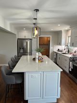 Modern kitchen with white island, stainless steel appliances, pendant lights, and gray bar stools.
