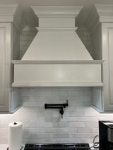 White kitchen range hood above stove, flanked by cabinets, with white tile backsplash.