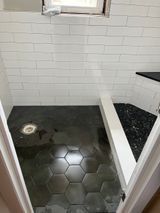 Bathroom with white tiled walls, hexagonal dark gray floor tiles, and a black countertop.