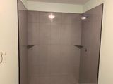 Empty gray tiled shower with two corner shelves and overhead lights.