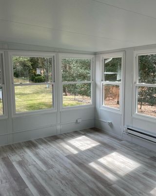 Empty sunroom with light wood-look flooring, multiple windows, and white walls and trim.