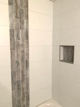 White tiled shower with a gray wood-look accent strip and a recessed shelf.