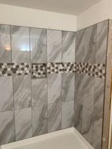 Gray tiled shower with a decorative mosaic band and a recessed niche.