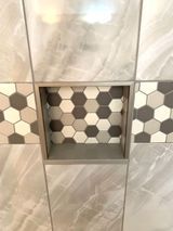Tile shower niche with hexagon-patterned interior, surrounded by large square tiles in various shades of gray.