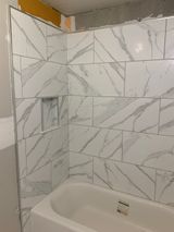 White marble-look tiles installed on a bathroom wall, with a built-in niche. A white tub is below.