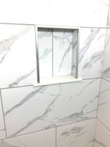White marble-look tiled shower with recessed shelf. Aluminum trim surrounds the niche.