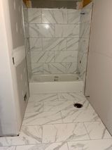 Bathroom under construction, with white marble-look tiles on the floor and in the shower surround, and a white tub.