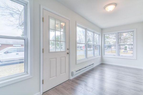 Sunroom with numerous windows, a door, white walls, and wood-look flooring.