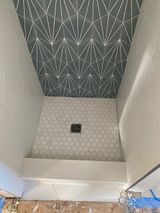 Shower with geometric tile ceiling in gray and white, hexagonal floor tile, and white walls.