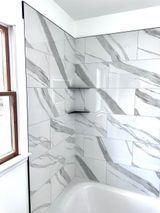 White marble-like tiled shower walls with gray veining, built-in shelf, next to a window.