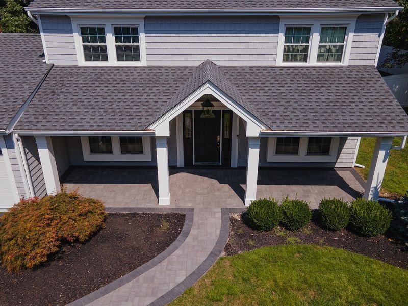 Gray house with a front porch, a dark door, windows, and a landscaped walkway.