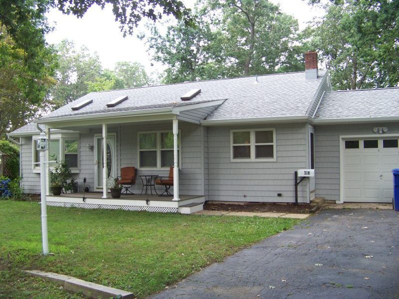 Gray one-story house with porch, garage, and driveway. Green lawn in front.