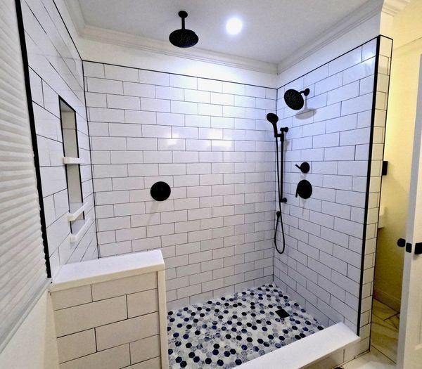 White tiled shower with black fixtures and pebble floor.