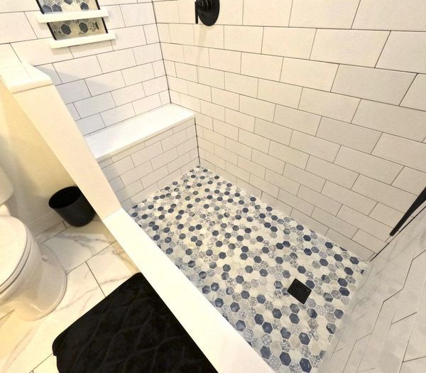 Bathroom shower with white subway tiles, a bench, and a blue and white pebble floor.