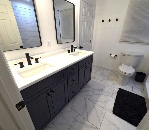 Modern bathroom with navy vanity, white countertop, marble tile floor, black fixtures.