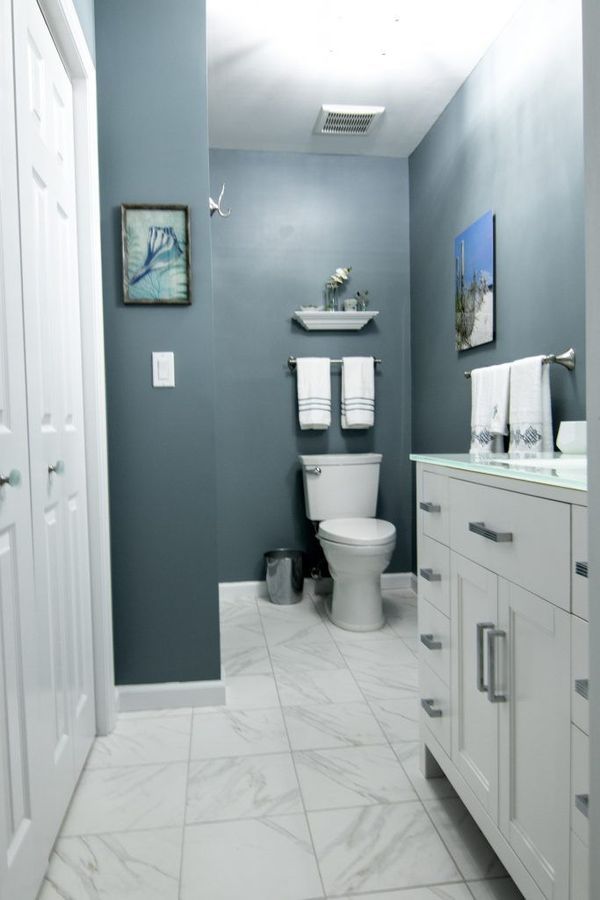 Blue-walled bathroom with white vanity, toilet, and towel rack. White marble-look tile floor.