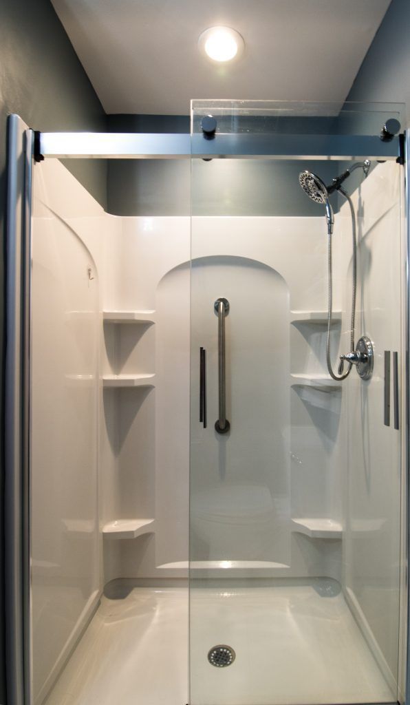 White accessible shower with glass door, handrail, built-in shelves, and a showerhead.