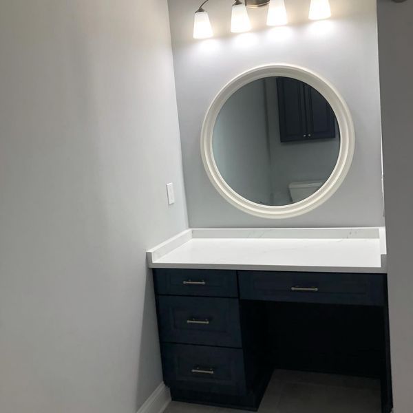 Bathroom vanity with navy blue cabinets, white countertop, and round mirror.