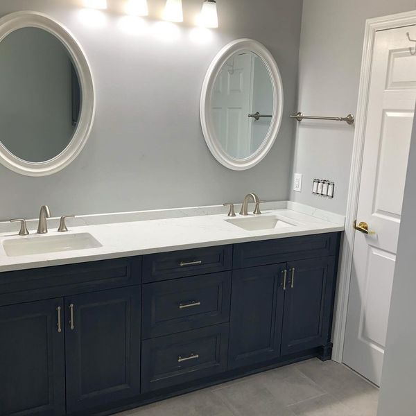 Bathroom with dual sinks, navy blue vanity, white countertop, oval mirrors, and gray walls.